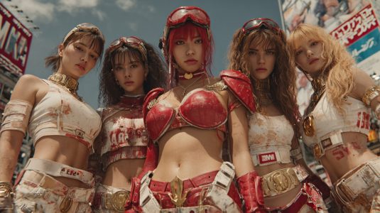 AI-generated K-pop idols in bold red and white armor — merging fashion, sci-fi, and stage aesthetics in one cinematic shot. Five K-pop-inspired performers wearing futuristic red and white armor-styled outfits posing together under a bright urban sky.